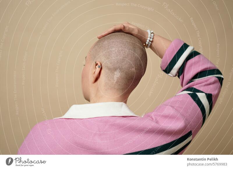 Back view of bald young woman touching head with no hair in studio, alopecia and cancer survivor concept female girl gen Z hair loss chemotherapy back view