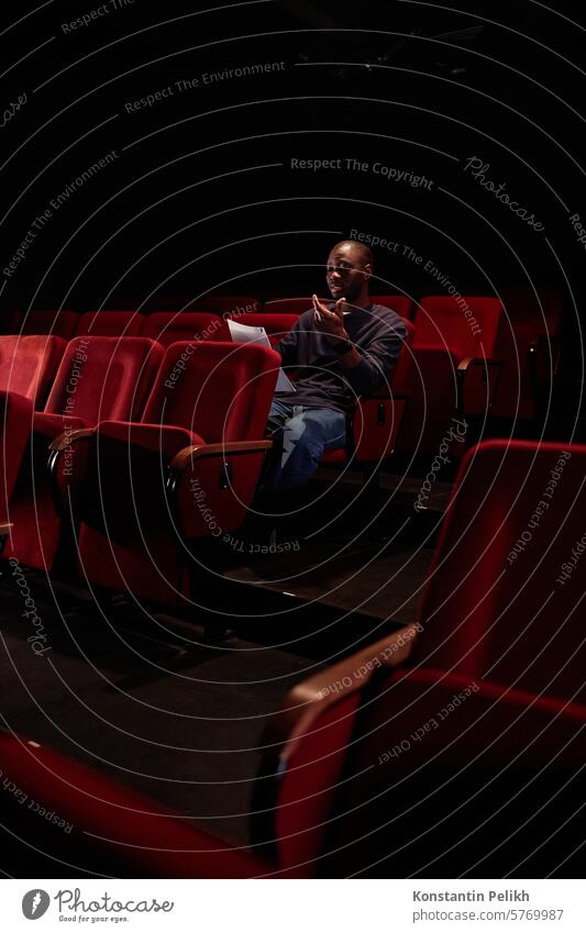 Vertical shot of African American man sitting in audience and reading lines before show in empty theater copy space artist performer actor Black man script