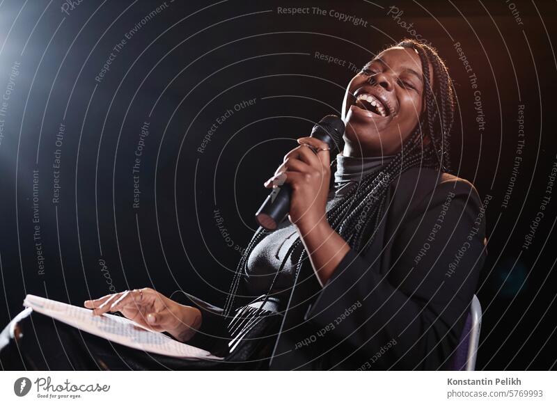 Portrait of Black woman laughing on stage and holding microphone while performing in comedy show copy space stand up talk show comic comedian artist performer