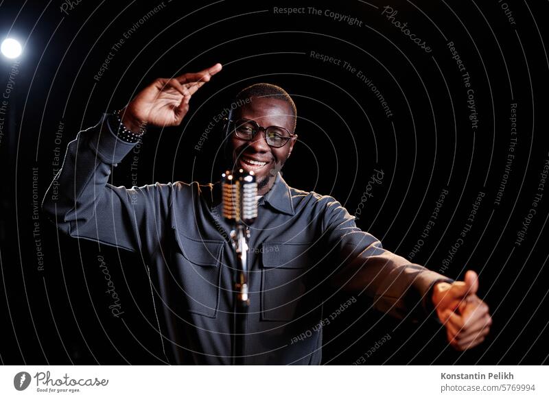 Minimal waist up portrait of emotional African American man speaking to microphone and performing on stage with spotlight copy space stand up comedy talk show