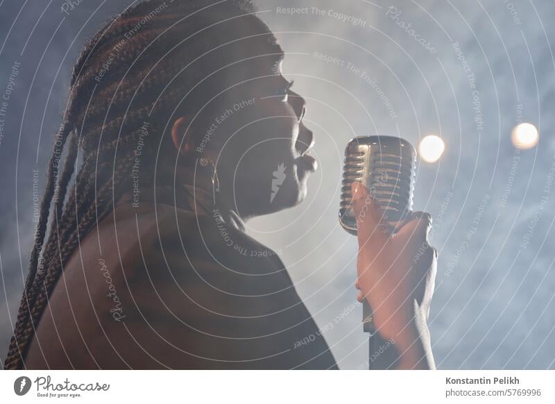 Side view portrait of African American woman singing to microphone on stage with smoke in background copy space song concert live music vocal artist performer