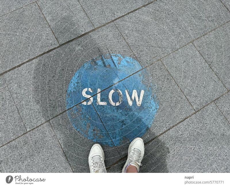 Top shot sidewalk with feet in front of painted SLOW icon. slow deceleration Slowly Sidewalk tempo Speed stress reduction stress management