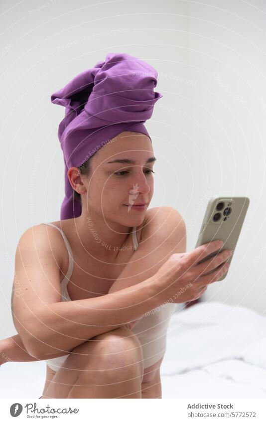 Woman with towel on head browsing phone after shower woman smartphone bed post-shower routine sitting bedroom phone screen towel wrap personal care relaxation