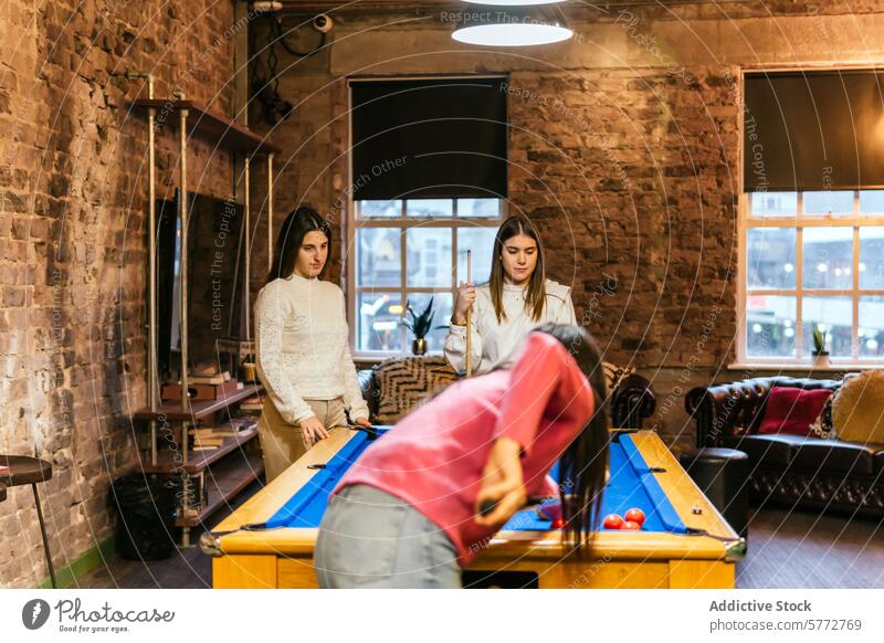 Young women friends enjoying a game of pool together young playing billiards leisure activity fun recreation cue balls table indoor cozy brick wall venue