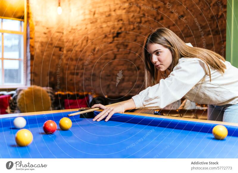 Young woman playing pool with friends in leisure time young billiard game indoor recreation playful table blue ball cue aim concentration focus shot casual cozy