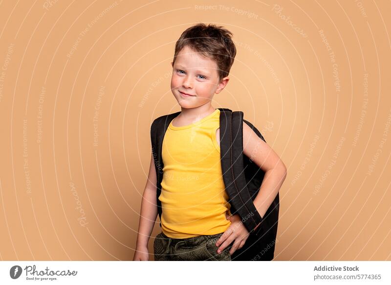 Confident young boy ready for school on beige background child backpack confident smile cheeky student yellow sleeveless shirt posing education schoolchild kid