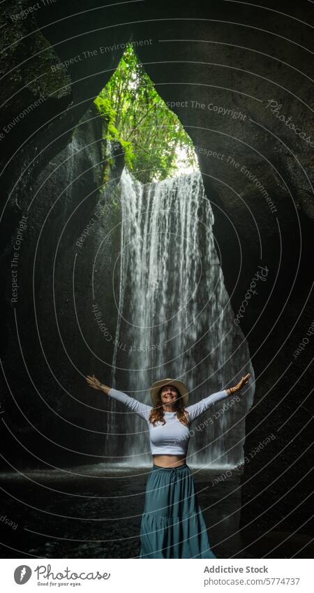Joyful woman embracing nature at Bali waterfall bali indonesia travel tourism joy arms outstretched hat green serene lush secluded enjoyment tranquility