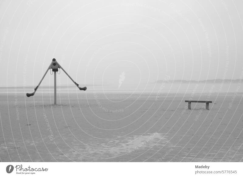 Abandoned playground equipment with bench in rain and storm at the beach playground on the beach of St. Peter-Ording in the district of Nordfriesland in Schleswig-Holstein in the fall on the North Sea coast in neo-realistic black and white