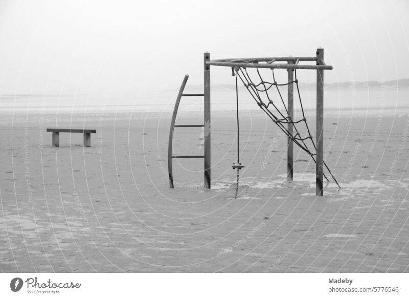 Abandoned climbing frame with bench in rain and storm at the beach playground on the beach of St. Peter-Ording in the district of Nordfriesland in Schleswig-Holstein in the fall on the North Sea coast in neo-realistic black and white