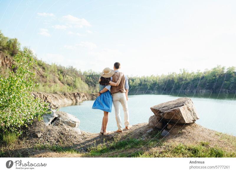 a young couple a guy and a girl are walking near a mountain lake surrounded dress blue stones spring summer love suit brown against the background perspective