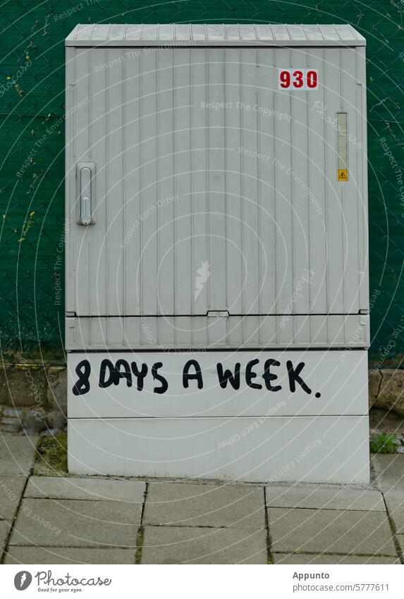 Restless "8 DAYS A WEEK" - lettering in black capital letters on the base of a light gray electrical distribution box (switch cabinet) in the outdoor area at the edge of a sidewalk