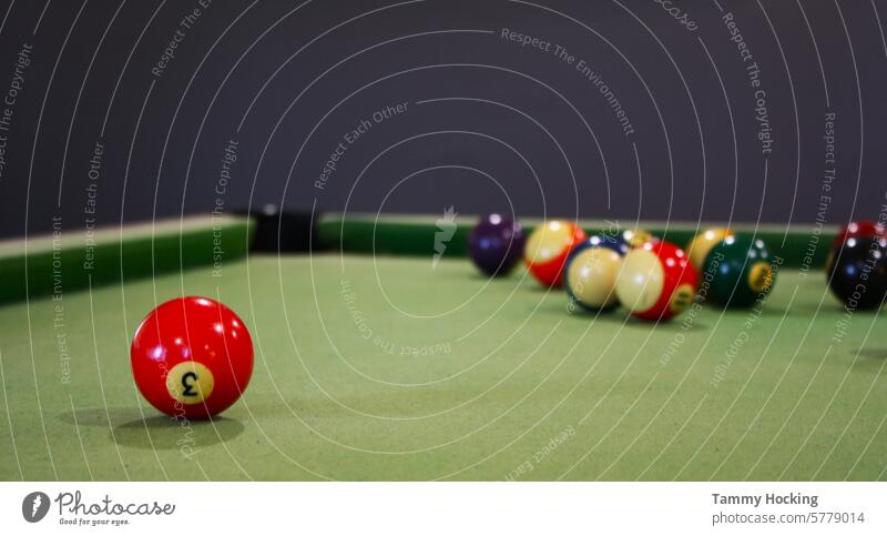 Scattering of pool balls after being hit by the white ball with the red ball in focus and the rest of the balls blurred in the background pool table number 3