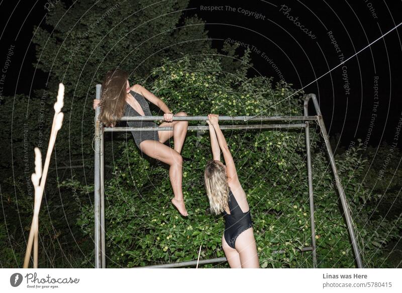 On a hot summer night, two gorgeous girls in swimsuits are having fun on the metal structures beneath the apple tree. These pretty and fit lingerie models are exercising while enjoying this perfect night. It might even seem like they’re sleepwalking.