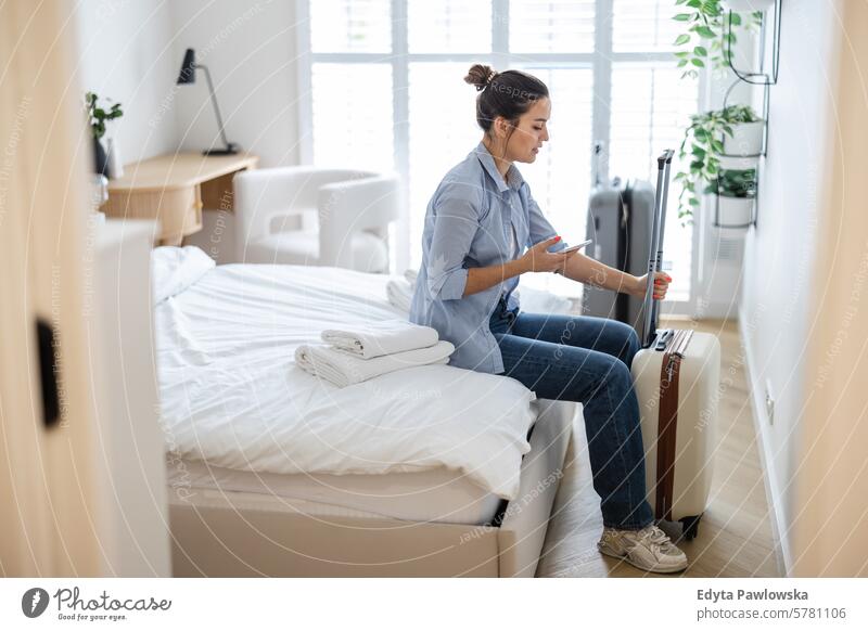 Young woman with a suitcase sitting on bed in hotel room and using phone packing clothing vacations travel preparation people luggage one person bag tourism