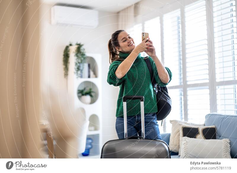 Young woman using mobile phone while standing with her suitcase in the hotel room packing clothing vacations travel preparation people luggage one person bag