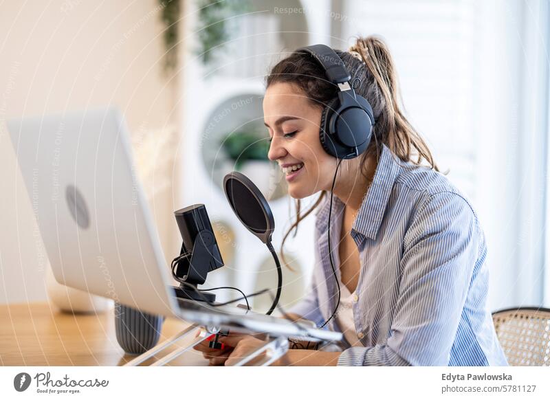 Woman wearing headphones sitting at a desk speaking into microphone and recording a podcast woman people one person room living room adult young young adult