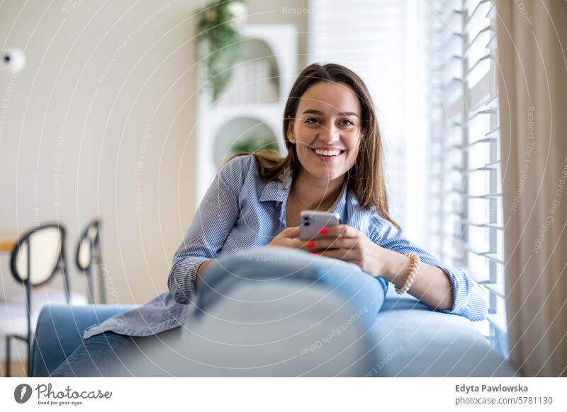 Smiling woman using mobile phone on sofa in living room at home people one person adult young young adult indoors apartment lifestyle happy smiling real people