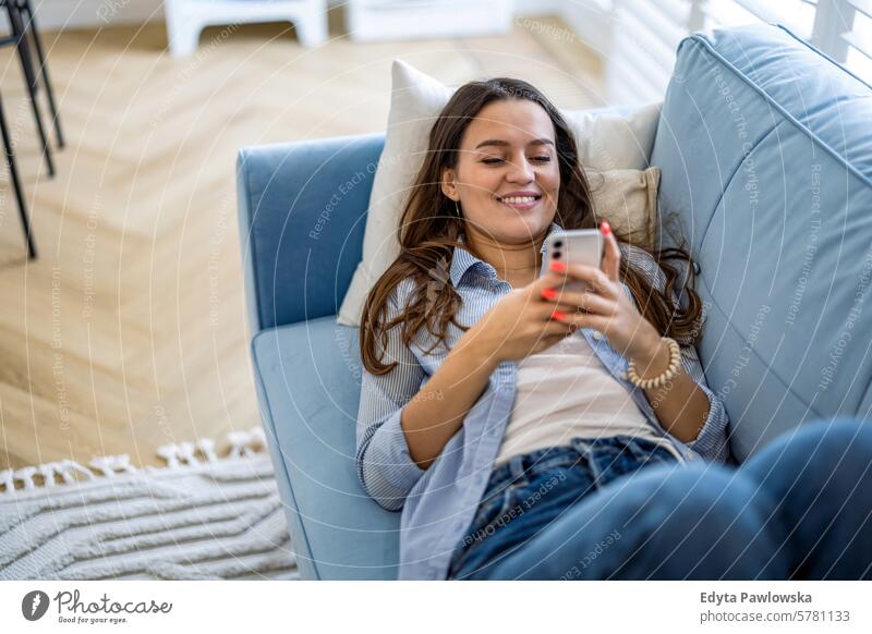 Smiling woman using mobile phone on sofa in living room at home people one person adult young young adult indoors apartment lifestyle happy smiling real people