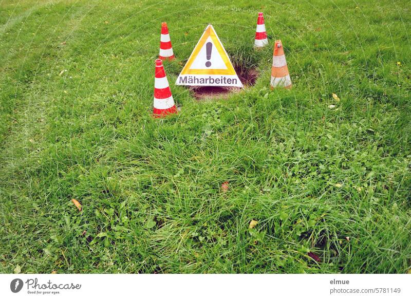 Foldable warning pyramid - mowing work - and four red and white warning cones on the meadow Warning pyramid mowing works Folding signal guiding cone danger spot