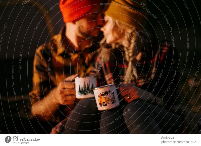 Young couple a guy and a girl in bright knitted hats stopped at a camping young beard warmth tent bonfire love get warm drink tea firewood blue orange cage