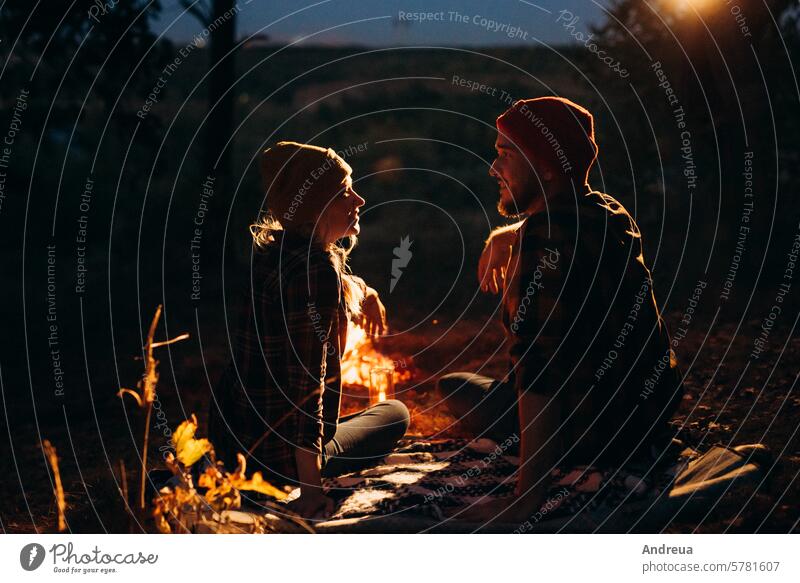 Young couple a guy and a girl in bright knitted hats stopped at a camping young beard warmth tent bonfire love get warm drink tea firewood blue orange cage