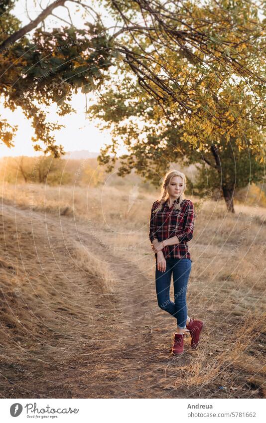 blonde with pigtails in a shirt, jeans, red shoes smiling girl laughs ground grass sunset autumn summer winter boots braids image model joy sit blue brown