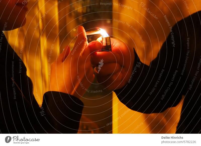 Night shot of young people in the cut: one hand gives fire to the other with a lighter Lighter open fire Cigarette Smoking Ignite Fire Nicotine young maiden
