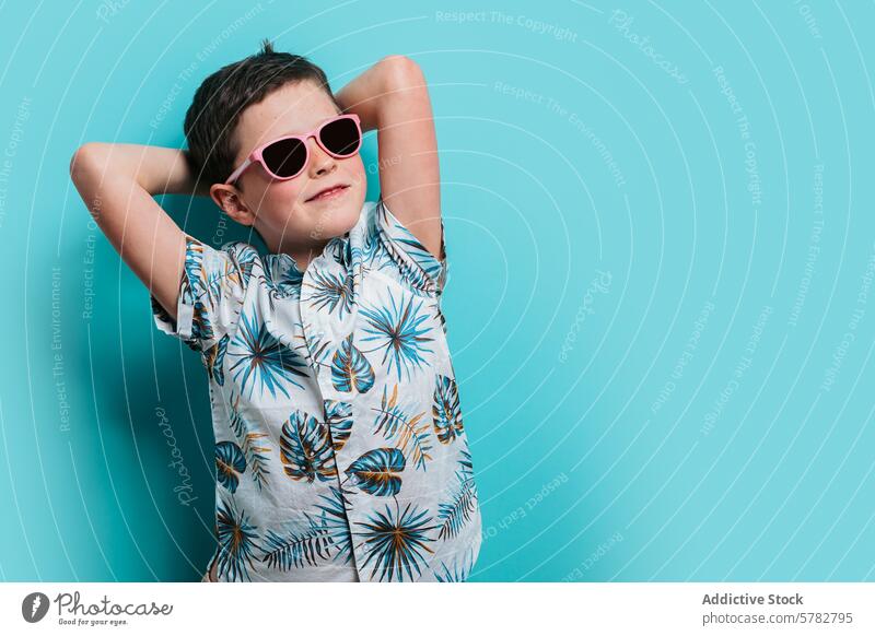 Young boy relaxing in tropical shirt and sunglasses child kid young relaxation casual pink leisure cheerful happy hands behind head teal background cool fashion