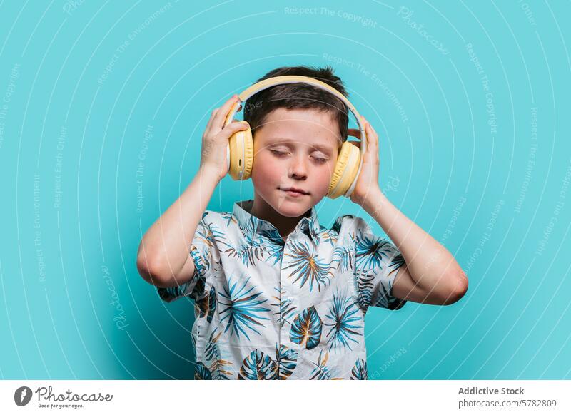 Young boy enjoying music with yellow headphones blue background floral shirt listening enjoyment child leisure audio sound closed eyes feeling young calm serene