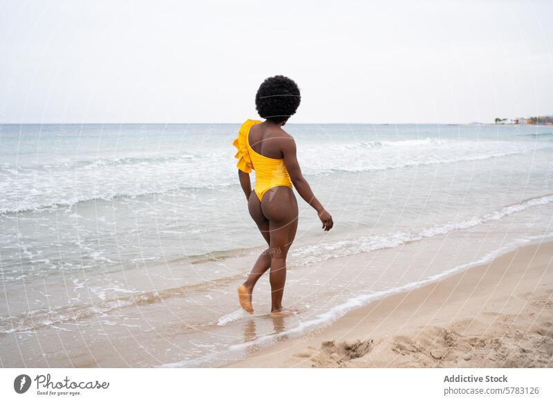 Woman in yellow swimsuit walking on the beach woman one-shoulder african leisure seashore wave sand water ocean vacation summer travel coastline outdoor