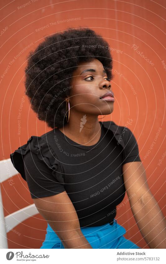 Contemplative Afro Woman in Casual Attire woman afro contemplative gaze distance black top blue trousers orange background young casual attire thoughtful