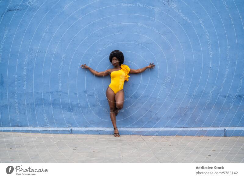Vibrant Afro Woman against Blue Wall in Yellow Outfit woman afro lifestyle fashion yellow blue wall pose confidence bold texture background swimsuit summer