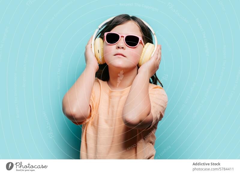Young girl enjoys music with headphones and sunglasses teal background fun style listening young child pink yellow enjoyment audio leisure entertainment