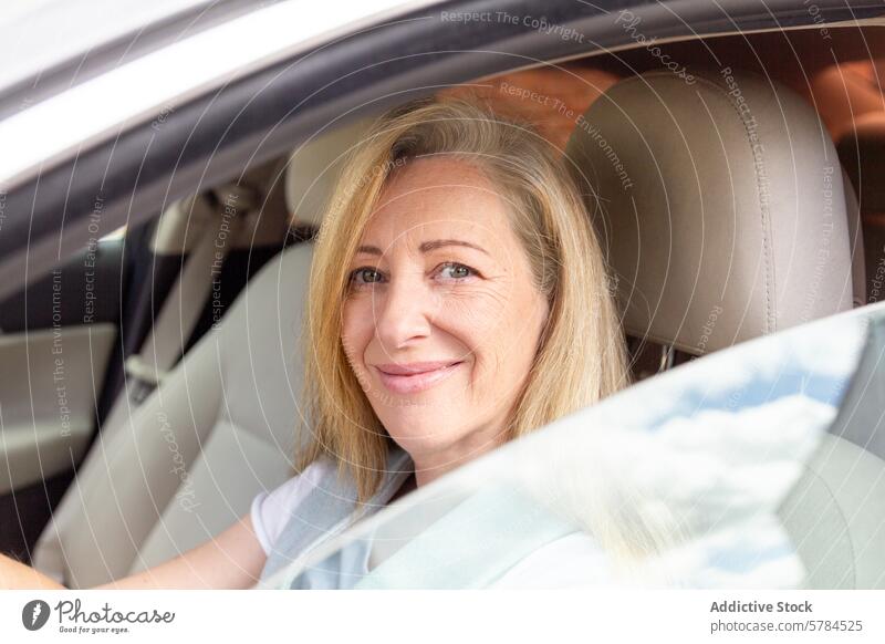 Mature woman smiling while sitting in a car mature smile driving driver seat blonde hair cheerful camera window vehicle adult female transport transportation