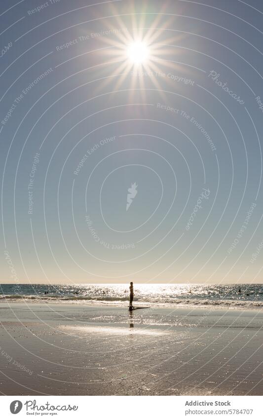 Serene beach scene with a person standing by the sea sun reflection solitary bright dazzling water sunlit horizon sky shore silhouette tranquil serene peaceful
