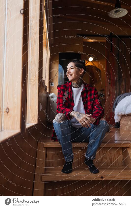 Serene woman enjoying a peaceful moment in a cabin tattoo casual smile window wooden tranquility contentment serene sitting red checkered shirt interior