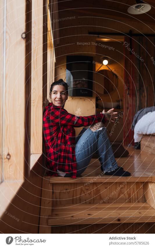 Young woman smiling on stairs in a cozy wooden cabin young rustic content casual sitting plaid shirt jeans happiness indoor leisure lifestyle simplicity