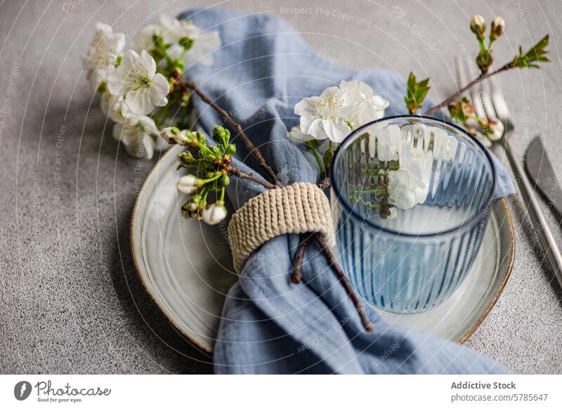 Elegant spring table setting with cherry blossoms branch plate glass striped napkin rustic texture background decor elegance serene fresh dining flower textile