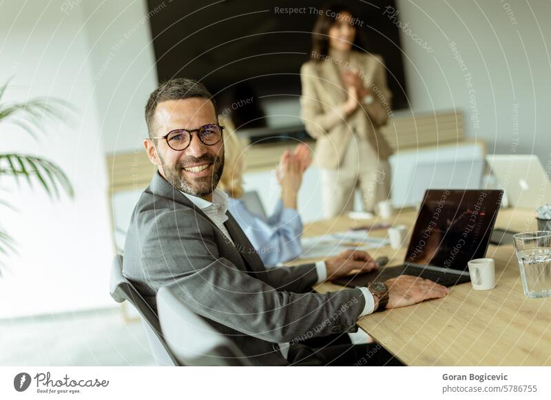 Smiling businessman in a modern office space enjoying a collaborative team meeting during work hours smiling colleagues collaboration eyeglasses laptop table