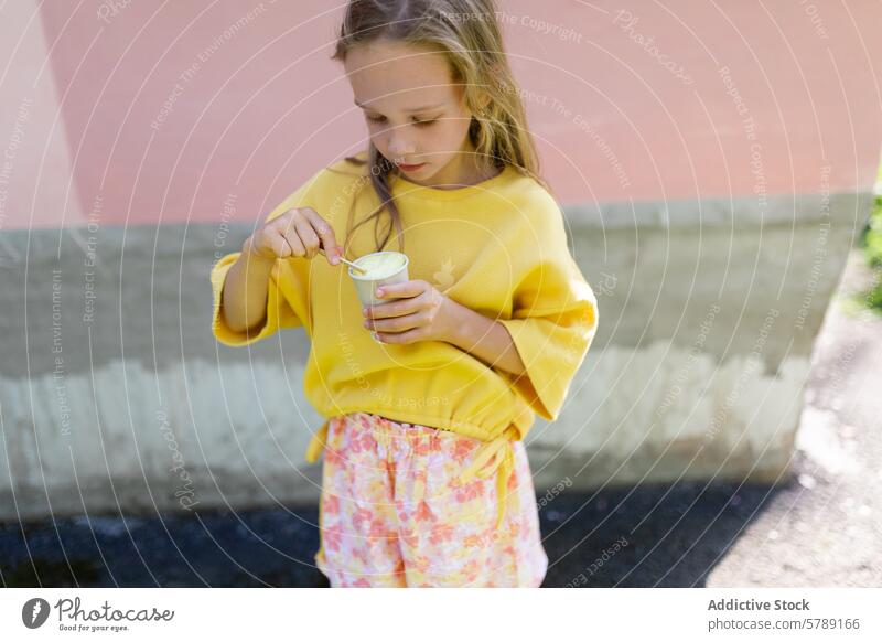 Young girl enjoying ice cream on sunny day young child eating blonde hair yellow sweater floral pants standing summer snack treat dessert leisure activity