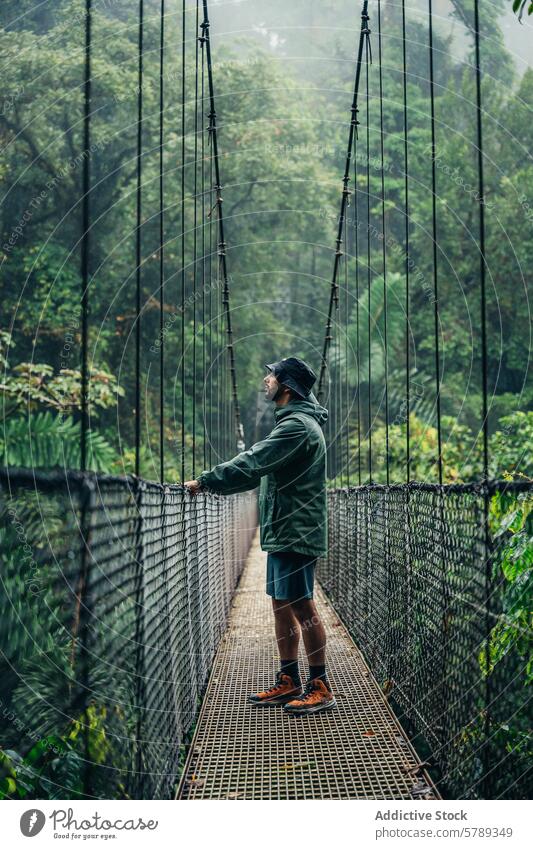 Man standing on a misty suspension bridge in Costa Rica costa rica man rainforest fog greenery lush nature outdoor adventure travel solitude reflection tranquil