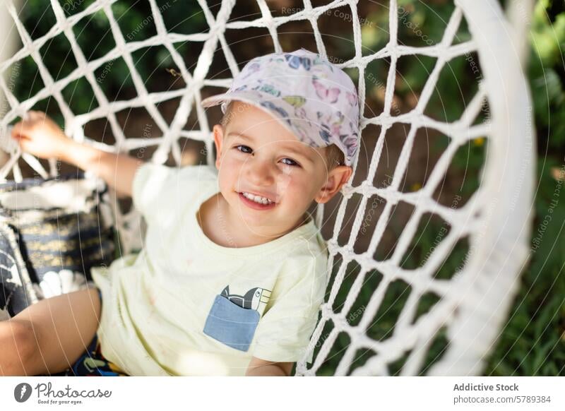 Joyful child playing on a swing in a garden joy smile cap outdoor sunny cheerful young sitting white enjoyment fun leisure casual kid happiness radiant nature