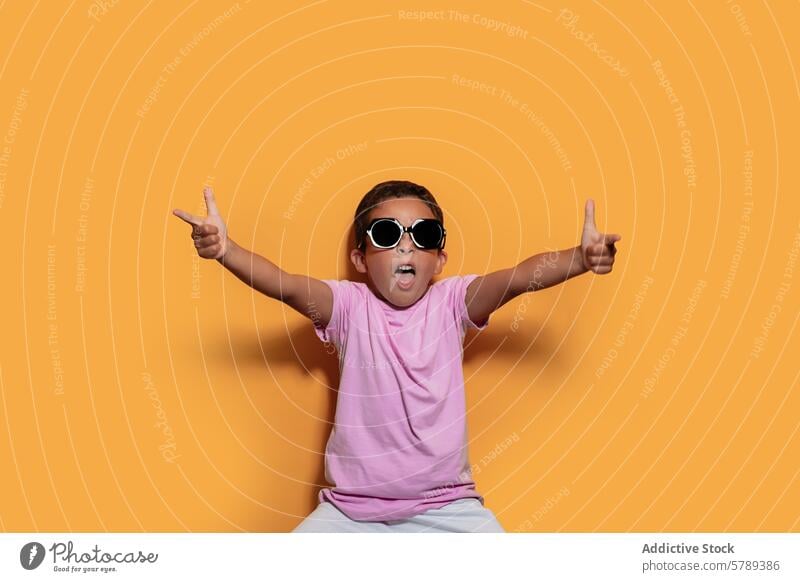 Excited child in sunglasses giving thumbs up studio excited joyful orange background pose kid happiness cheerful fun gesture approval fashion style bright
