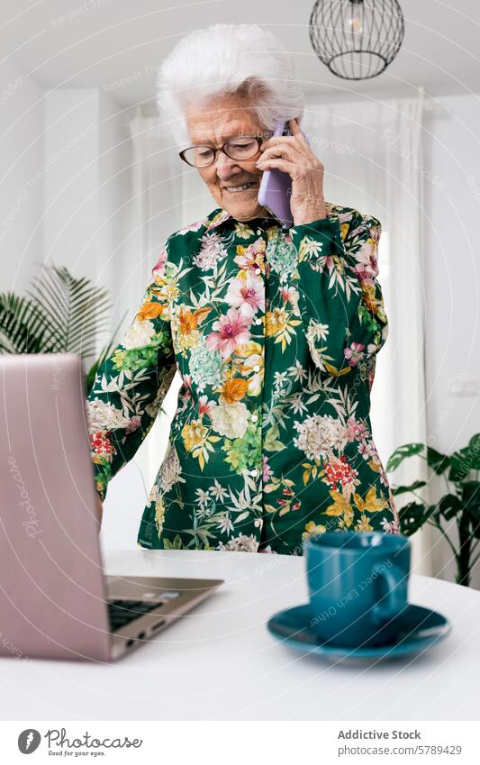 Senior woman multitasking at home with technology senior elderly working laptop phone conversation blouse floral interior domestic house fashionable style