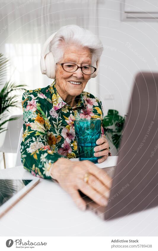 Senior woman working on laptop at home with headphones senior technology smile elderly active aging floral shirt glasses computer digital internet online