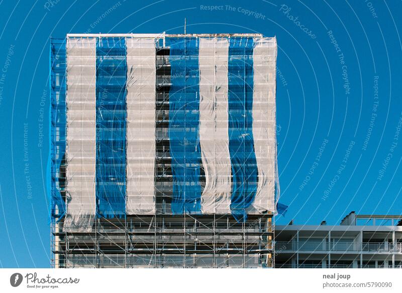 Scaffolding covered with blue and white striped gauze against a bright blue sky Architecture Construction site Geometry graphically structure color blocking