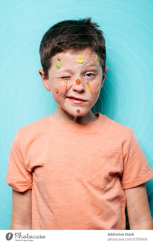 Boy with playful fruit stickers on his face boy happy teal background posing young cute colorful adhesive facial expression child decoration casual clothing