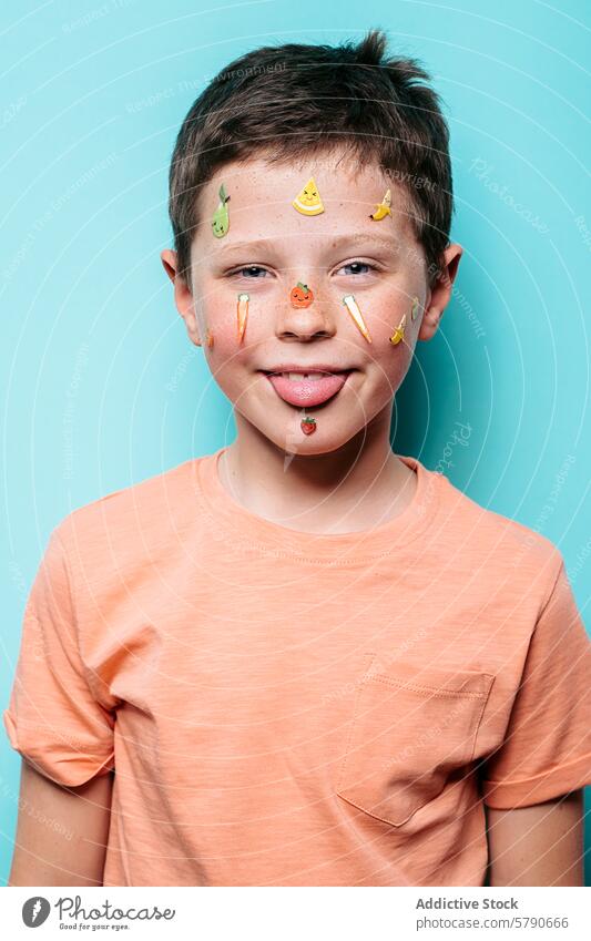 Cheerful boy with fruity stickers on face and tongue out child cheerful joy playful colorful turquoise background youthful fun peach smile casual shirt pocket