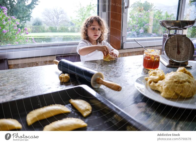 Young child baking in a kitchen with rolling pin and dough pastry kneading concentrate curly hair sunny home cooking homemade domestic life childhood culinary