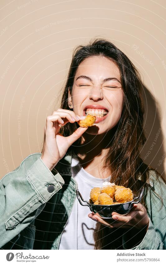 Cheerful young woman enjoying fried cheese balls cheerful eating snack crispy delicious food bowl pleasure taste bite casual clothing green jacket white t-shirt